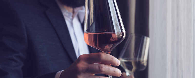 Mann im Sakko hält Weinglas mit Rotwein in der Hand